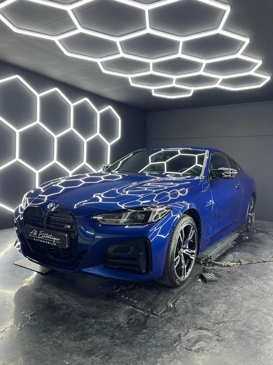 BMW M240i bleue, vue 3/4 avant sous l’éclairage hexagonal de l’atelier