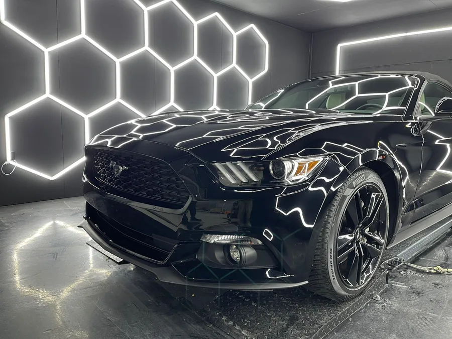 Ford Mustang GT noire, vue 3/4 avant sous l’éclairage hexagonal de l’atelier